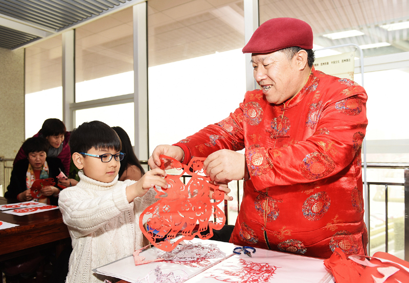 2月7日,在山东胶州市文化馆"新春非遗展"现场,一名剪纸艺人把剪纸作品